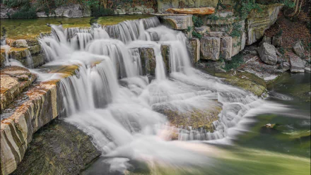 HD desktop wallpaper of a cascading waterfall flowing over rocky tiers surrounded by lush greenery.