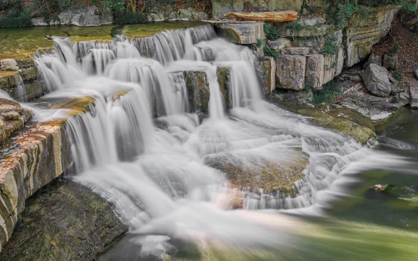 HD desktop wallpaper of a cascading waterfall flowing over rocky tiers surrounded by lush greenery.