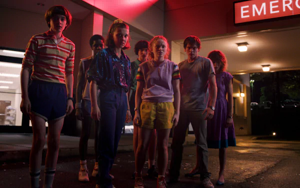 HD desktop wallpaper featuring characters from the TV show Stranger Things standing together outside a brightly lit building with an 'Emergency' sign.