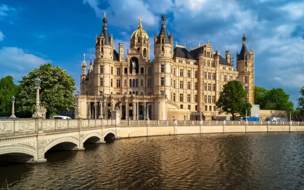 HD PC desktop wallpaper of Schwerin Palace, a majestic man-made castle reflected in the water under a vibrant blue sky.