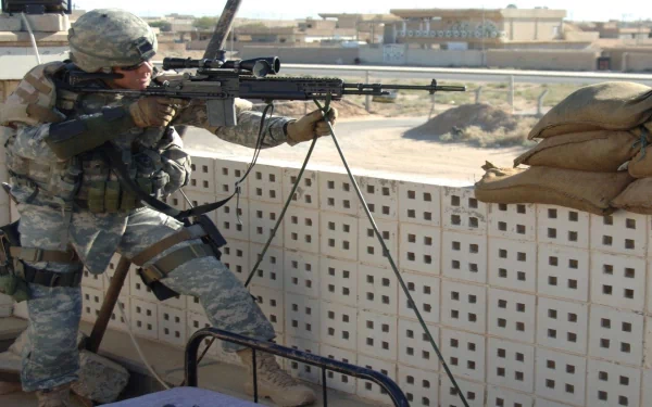 A high-definition desktop wallpaper featuring a military sniper in camouflage gear, aiming a rifle from behind a barricade with sandbags, against an urban backdrop. Tags: supersnipersal, army, military, sniper.
