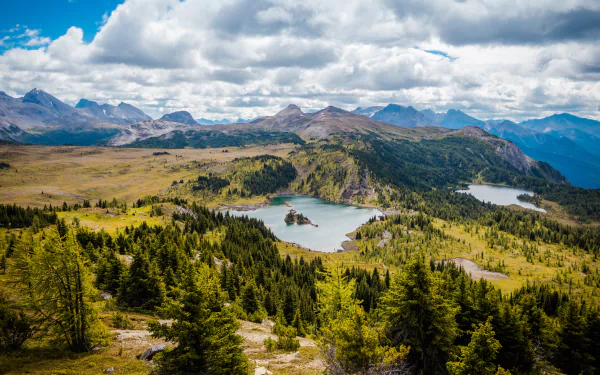 HD desktop wallpaper and background showcasing a beautiful landscape with a serene lake nestled among green hills and mountains under a partly cloudy sky.