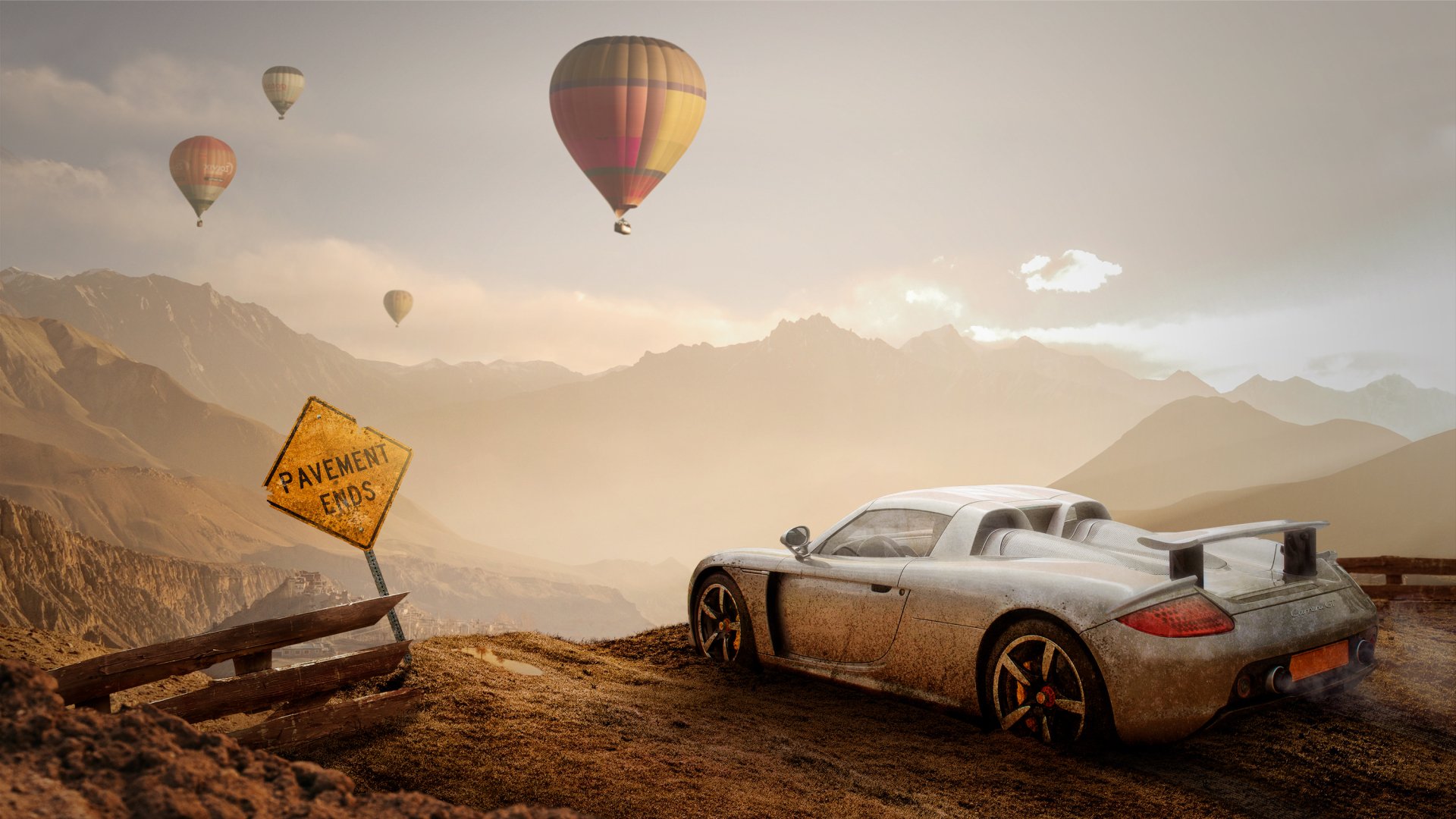 2K Quad HD PC desktop wallpaper: Porsche Carrera GT parked on a mountain overlook at sunrise, hot air balloons drifting over rugged peaks, weathered road sign and panoramic vehicle view.