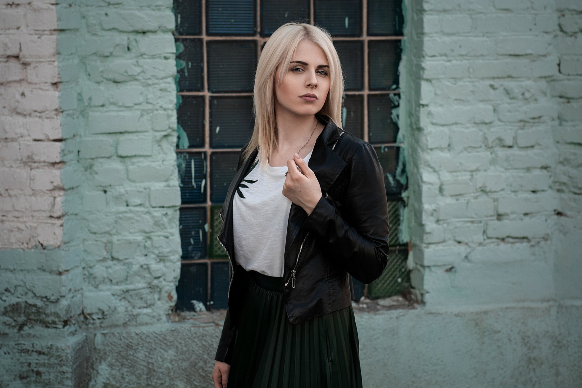 Blonde woman model wearing a black leather jacket and white shirt stands confidently against a textured brick wall, captured in an HD PC desktop wallpaper background.