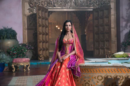 HD wallpaper of British actress Naomi Scott as Princess Jasmine in a pink dress from the 2019 movie Aladdin, featuring her black hair and brown eyes in a royal setting.