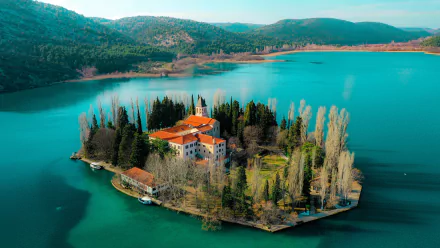 A serene aerial view of Visovac Monastery, nestled on an island in Croatia, surrounded by lush trees and clear blue water, showcasing its tranquil beauty and spiritual significance.