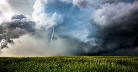 HD PC desktop wallpaper of a tornado forming over a green field beneath dramatic storm clouds in a striking natural landscape.