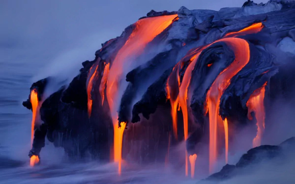 HD wallpaper featuring molten lava flowing down a volcanic rock formation, surrounded by misty clouds. The natural scene vividly captures the raw power and beauty of an active volcano.