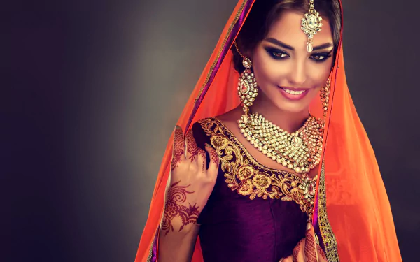 4K Ultra HD PC desktop wallpaper of a smiling Indian model in a saree — black hair, brown eyes, ornate necklace and earrings, mehndi on her hand and a vibrant orange veil.