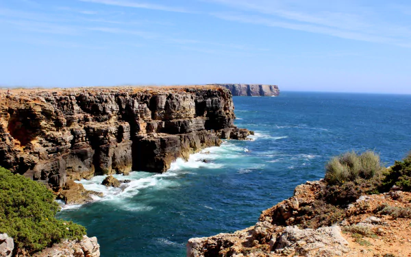 4K Ultra HD desktop wallpaper capturing Portugal’s rugged coastline where rocky cliffs meet the deep blue ocean under a clear sky, showcasing nature’s raw beauty.