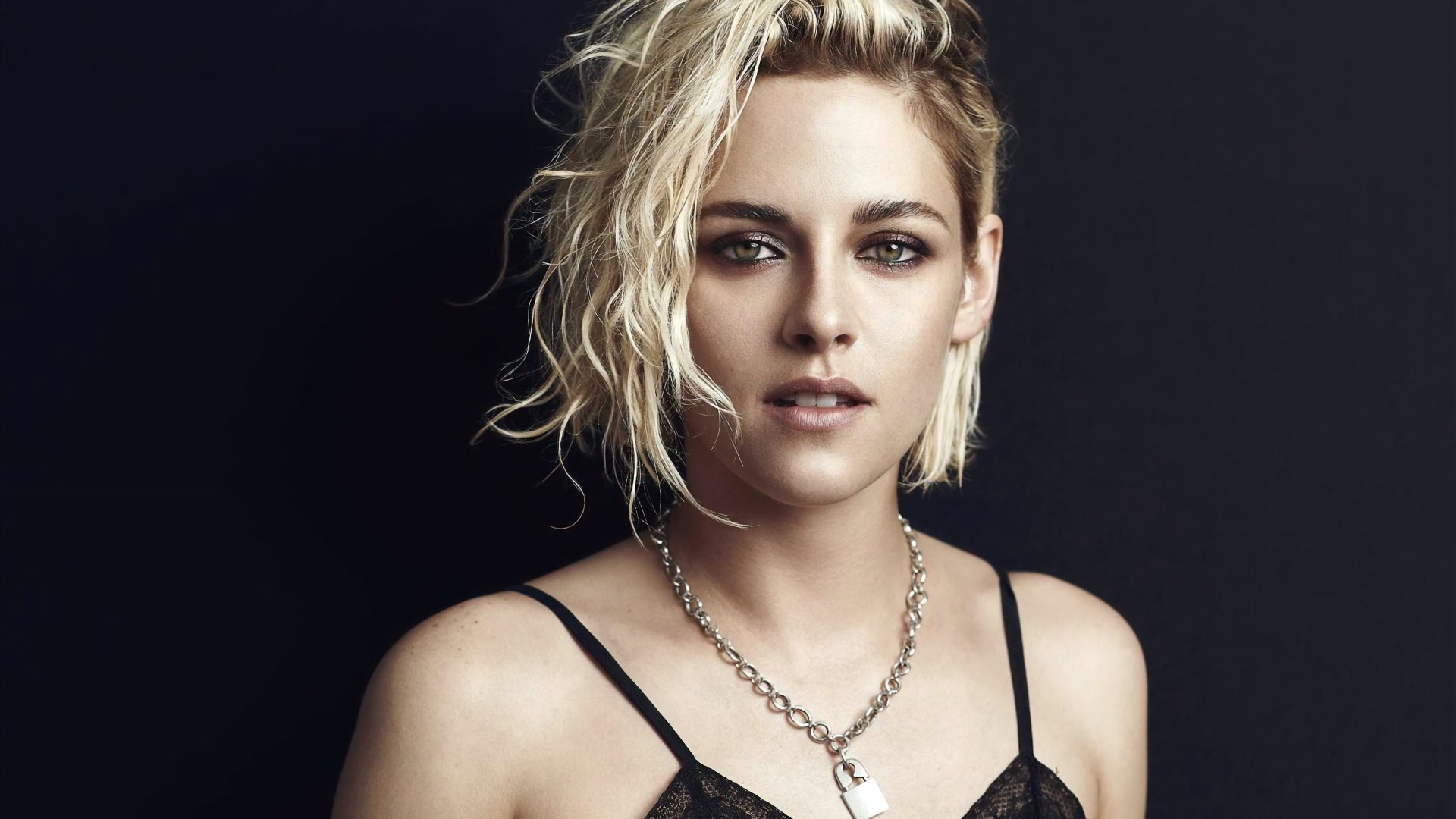 4K desktop wallpaper: close-up portrait of a short blonde with tousled hair and striking green eyes, wearing a chain necklace against a dark background.