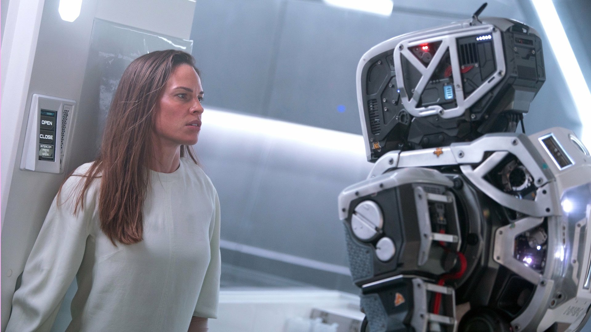 Hilary Swank confronts a robotic figure in a scene from the movie I Am Mother. This HD desktop wallpaper captures a tense moment in a futuristic setting.