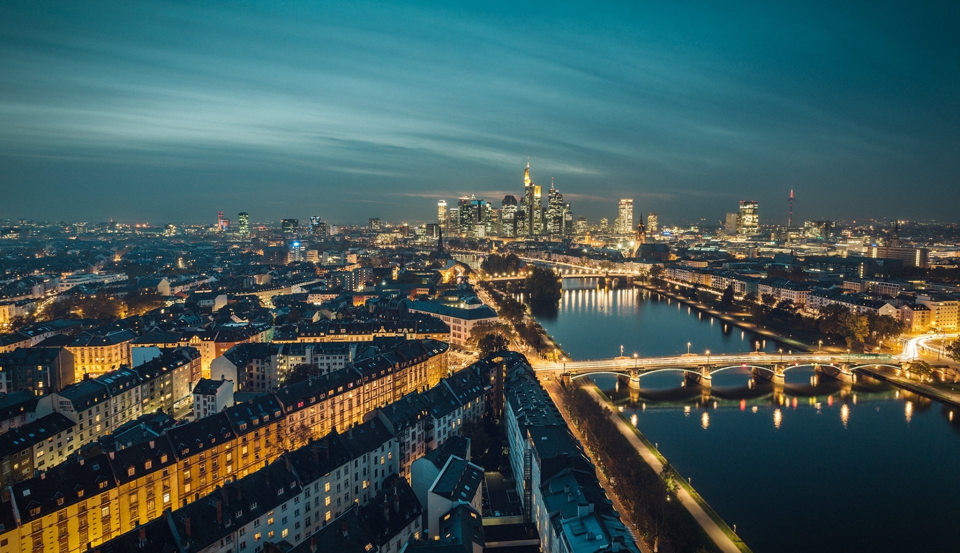 Aerial night view of Frankfurt, Germany — illuminated bridges and riverside buildings reflecting city lights on the river; man-made skyline HD desktop wallpaper background.