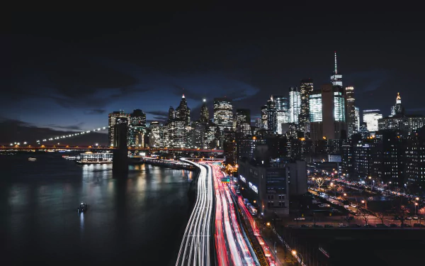 Nighttime 4K Ultra HD cityscape of Manhattan, New York, featuring the illuminated Brooklyn Bridge with vibrant light trails under a dark sky in a time-lapse style.