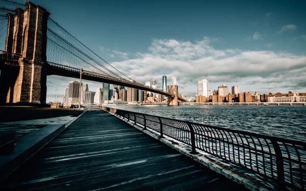 HD desktop wallpaper of the Brooklyn Bridge spanning the East River with the New York City skyline in the background under a partly cloudy sky.