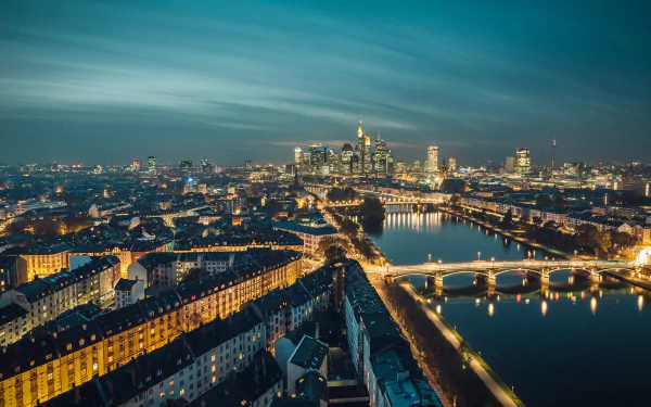 Aerial night view of Frankfurt, Germany — illuminated bridges and riverside buildings reflecting city lights on the river; man-made skyline HD desktop wallpaper background.