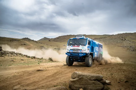 Red Bull Kamaz rallying vehicle kicks up sand across rugged terrain in a sports event — 5K Ultra HD PC desktop wallpaper background.