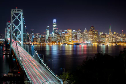 8K Ultra HD PC desktop wallpaper of a man-made cityscape: illuminated Bay Bridge stretching toward a glittering night skyline reflected on the bay.