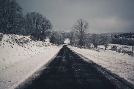 A snowy, man-made road stretches through a winter landscape under a cloudy sky, captured in 4K Ultra HD for a PC desktop wallpaper.