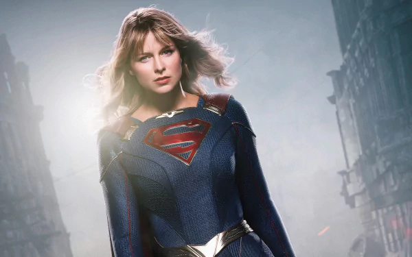 Supergirl (TV Show) 2K Quad HD desktop wallpaper: woman in blue-and-red Supergirl costume with S-shield stands resolute against a misty, ruined city skyline.