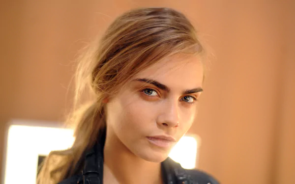 Close-up portrait of a blonde woman with blue eyes against a warm blurred background, styled as a 2K Quad HD PC desktop wallpaper.