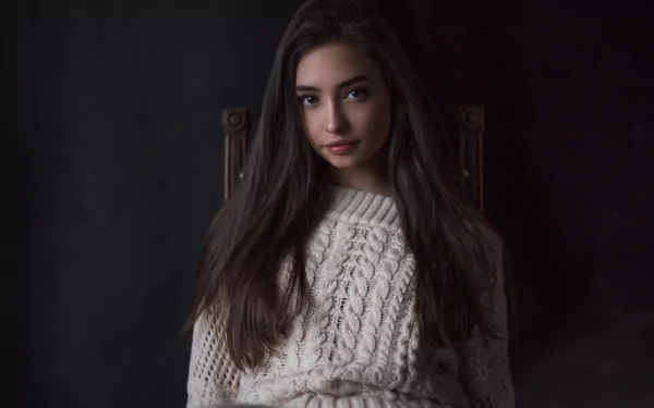 HD PC wallpaper of a long-haired woman model with black hair and a soft face, wearing a cream cable-knit sweater against a dark, moody background.
