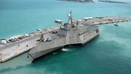 The USS Independence (LCS-2) is a littoral combat ship docked at a pier, showcasing its modern military design against a vibrant turquoise sea.