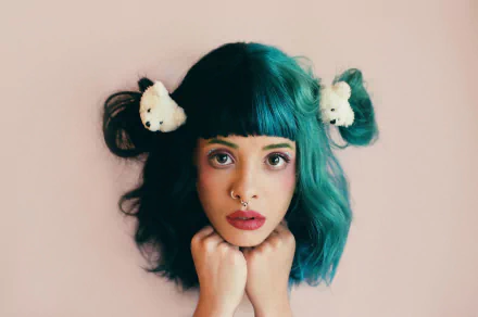 HD desktop wallpaper featuring American singer Melanie Martinez with teal hair styled in buns adorned with white accessories, wearing bold lipstick against a soft background.