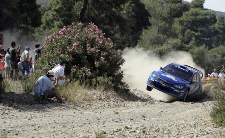 HD PC desktop wallpaper featuring a Subaru WRC racing car kicking up dust on a rugged dirt track, surrounded by spectators and lush greenery.