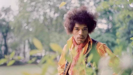 HD desktop wallpaper featuring Jimi Hendrix outdoors, surrounded by soft greenery, capturing the iconic musician with a serene expression and his guitar nearby.