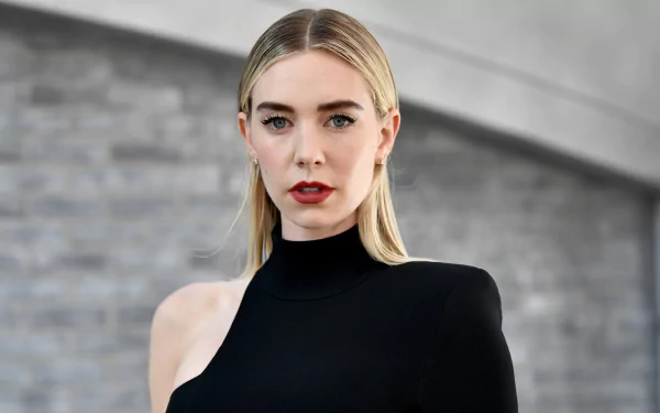 HD desktop wallpaper featuring English actress Vanessa Kirby with blonde hair, blue eyes, and red lipstick, wearing a stylish black outfit against a blurred gray background.