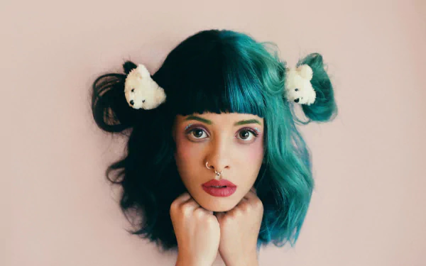 HD desktop wallpaper featuring American singer Melanie Martinez with teal hair styled in buns adorned with white accessories, wearing bold lipstick against a soft background.