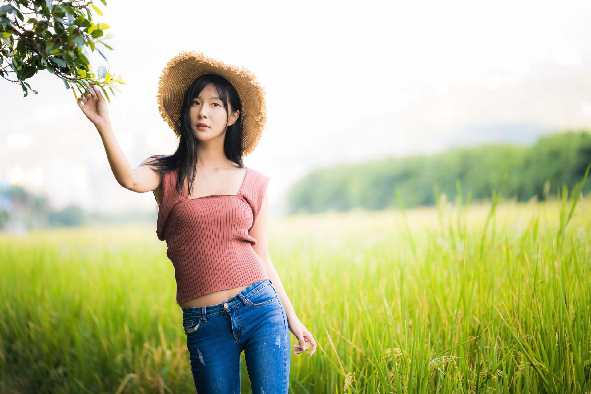 Asian woman with black hair wearing a hat and pink top stands in a green field, captured with shallow depth of field in 4K Ultra HD resolution.