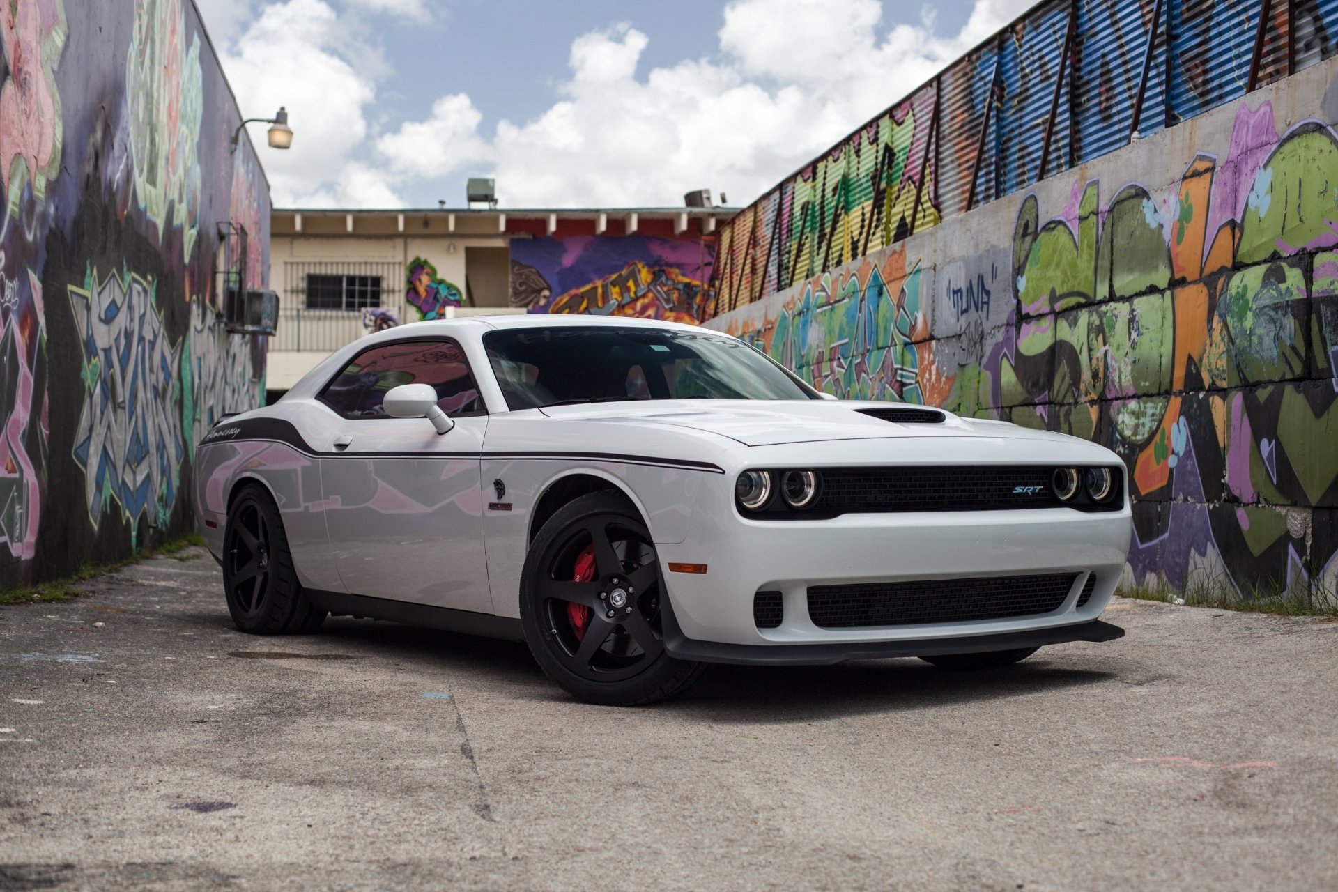 White Dodge Challenger SRT Hellcat muscle car parked in an urban alley with vibrant graffiti walls, showcased in a high-definition PC desktop wallpaper.