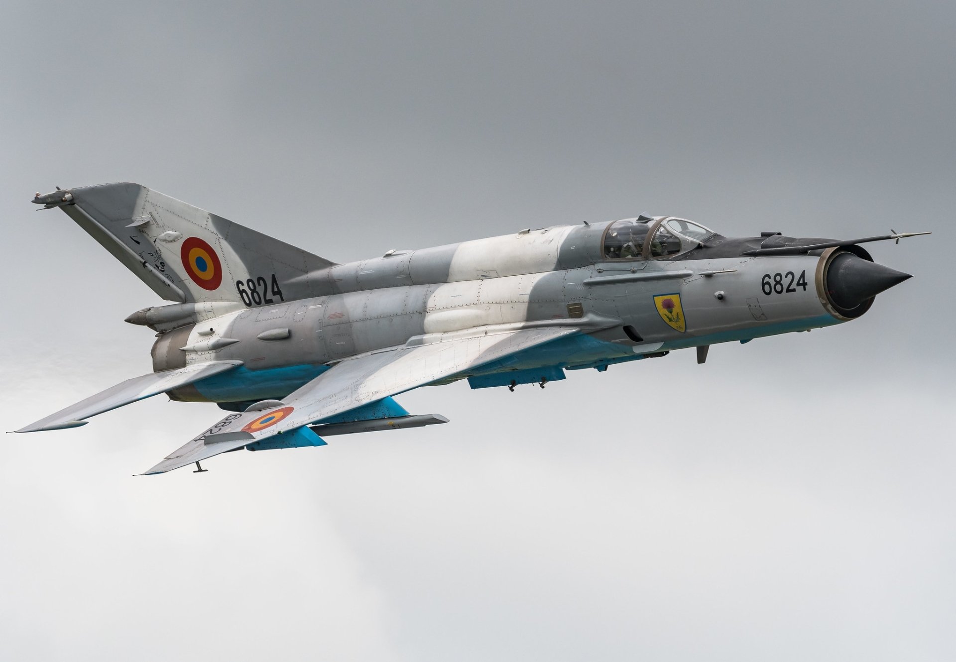 HD desktop wallpaper featuring a Mikoyan-Gurevich MiG-21 jet fighter warplane in flight, showcasing its military aircraft design against a cloudy sky.