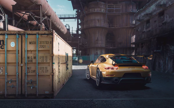 HD wallpaper featuring a Porsche 997 Porsche 911 GT2 RS parked in an industrial setting, surrounded by large metal structures and containers.