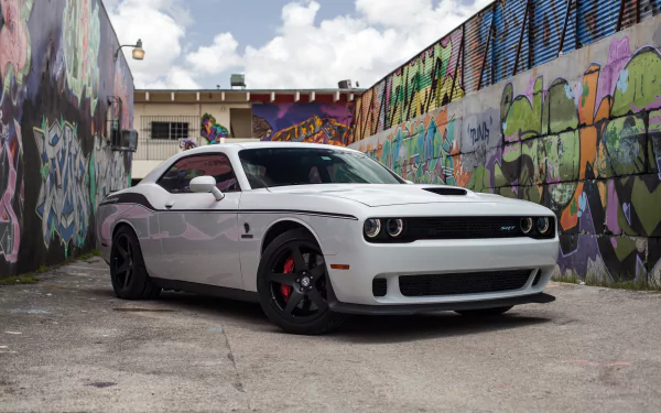 White Dodge Challenger SRT Hellcat muscle car parked in an urban alley with vibrant graffiti walls, showcased in a high-definition PC desktop wallpaper.