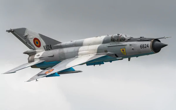HD desktop wallpaper featuring a Mikoyan-Gurevich MiG-21 jet fighter warplane in flight, showcasing its military aircraft design against a cloudy sky.
