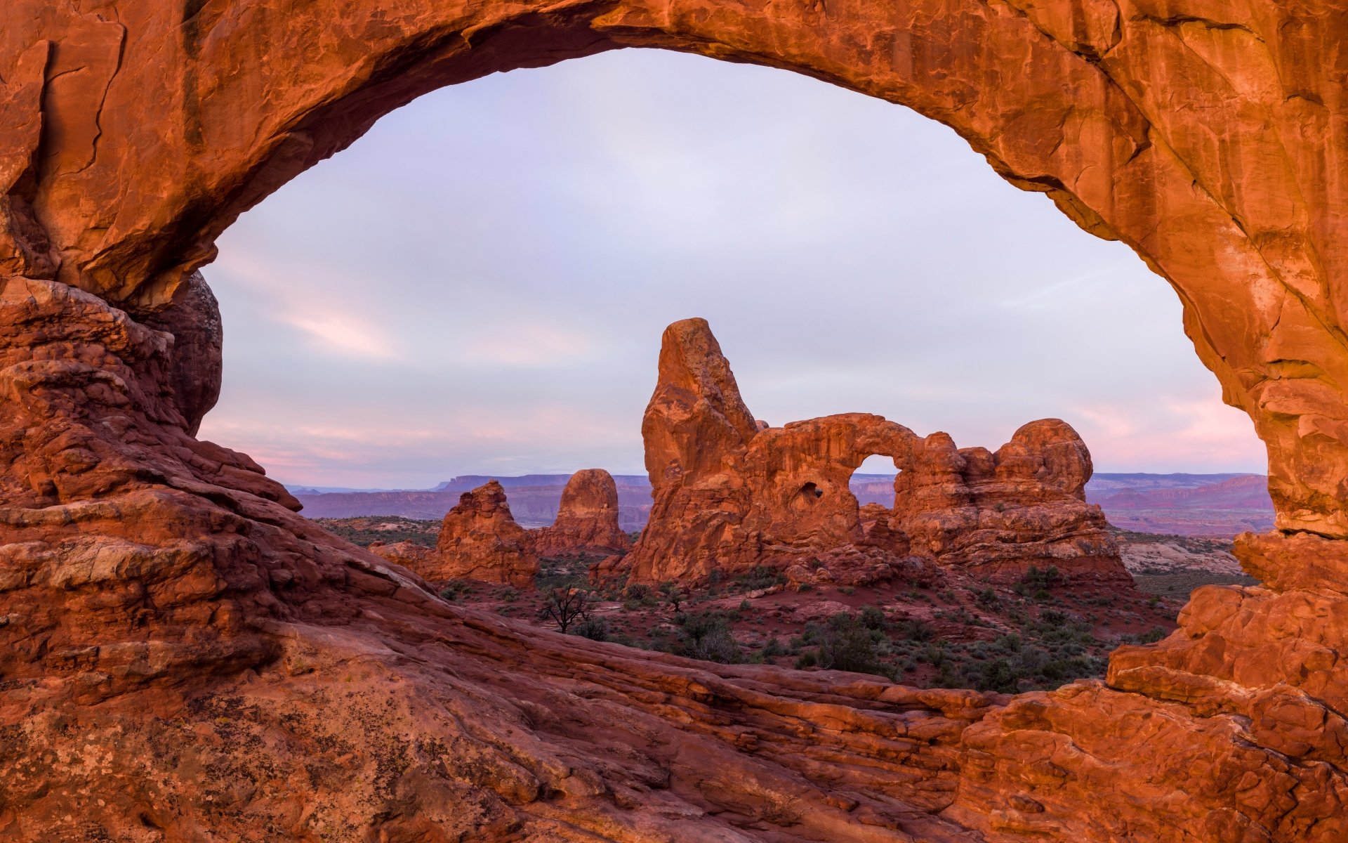 8K Ultra HD view of a natural sandstone arch framing the desert landscape of Arches National Park, Utah, USA, highlighting the region’s unique rock formations at sunset.