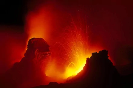 HD PC desktop wallpaper of a dramatic nature scene: an erupting volcano with molten lava, fiery plumes and silhouetted rock formations.