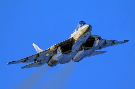 Sukhoi Su-57 jet fighter, a sleek military warplane, soars against a clear blue sky in this HD PC desktop wallpaper and background.