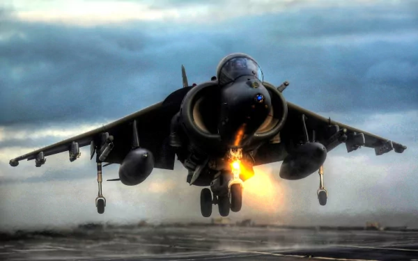 McDonnell Douglas AV-8B Harrier II military jet taking off with vertical-thrust flames over a runway beneath dramatic clouds — 2K Quad HD PC desktop wallpaper/background.