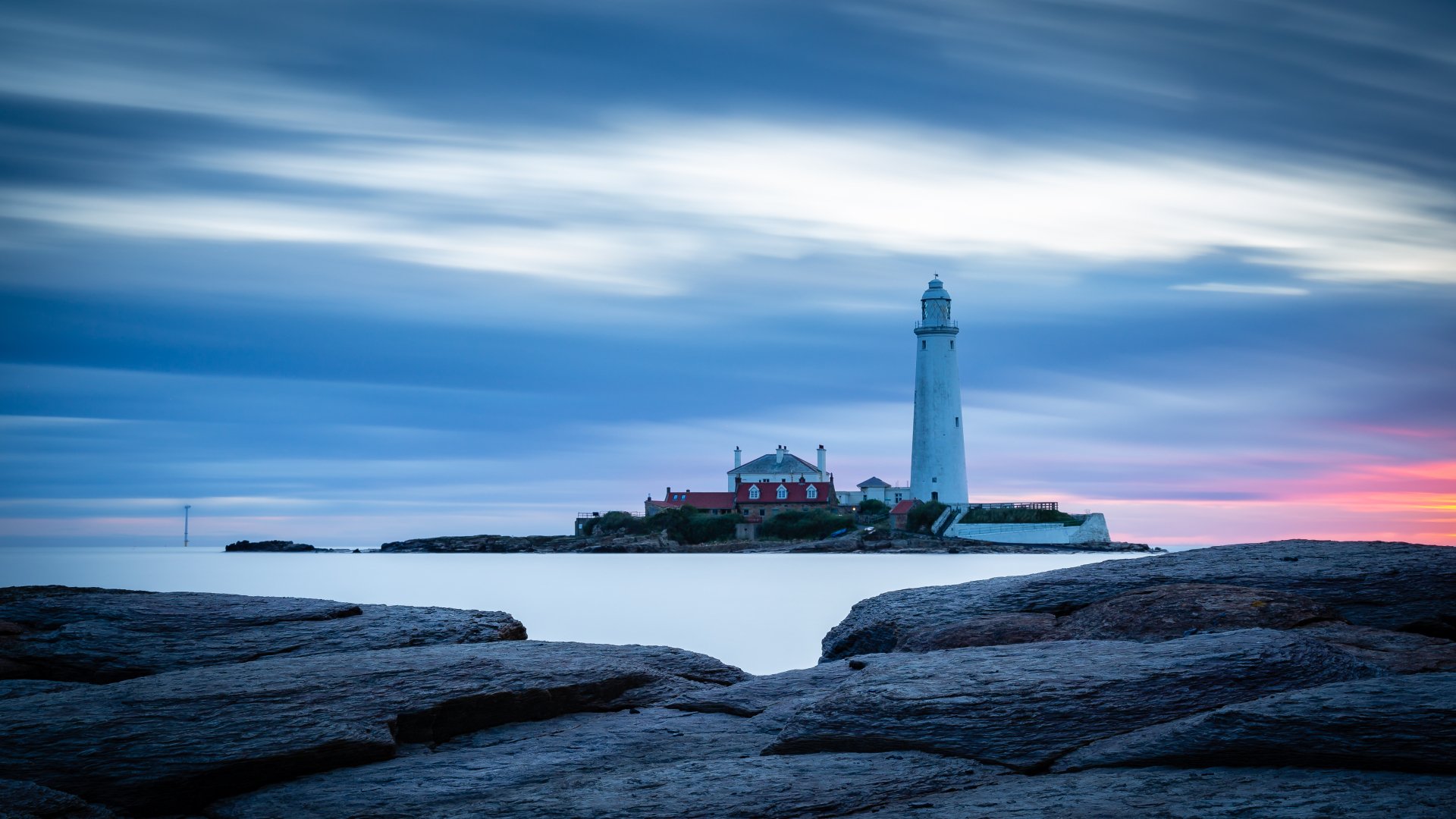 4K Ultra HD desktop wallpaper featuring a man-made lighthouse on a rocky shore under a serene, cloudy sky at dusk.