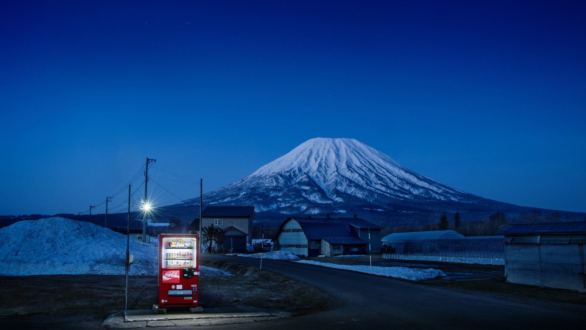 A serene Japan mountain scene at dusk with snow-covered peaks, illuminated buildings, and a bright vending machine, captured in stunning 4K Ultra HD photography.