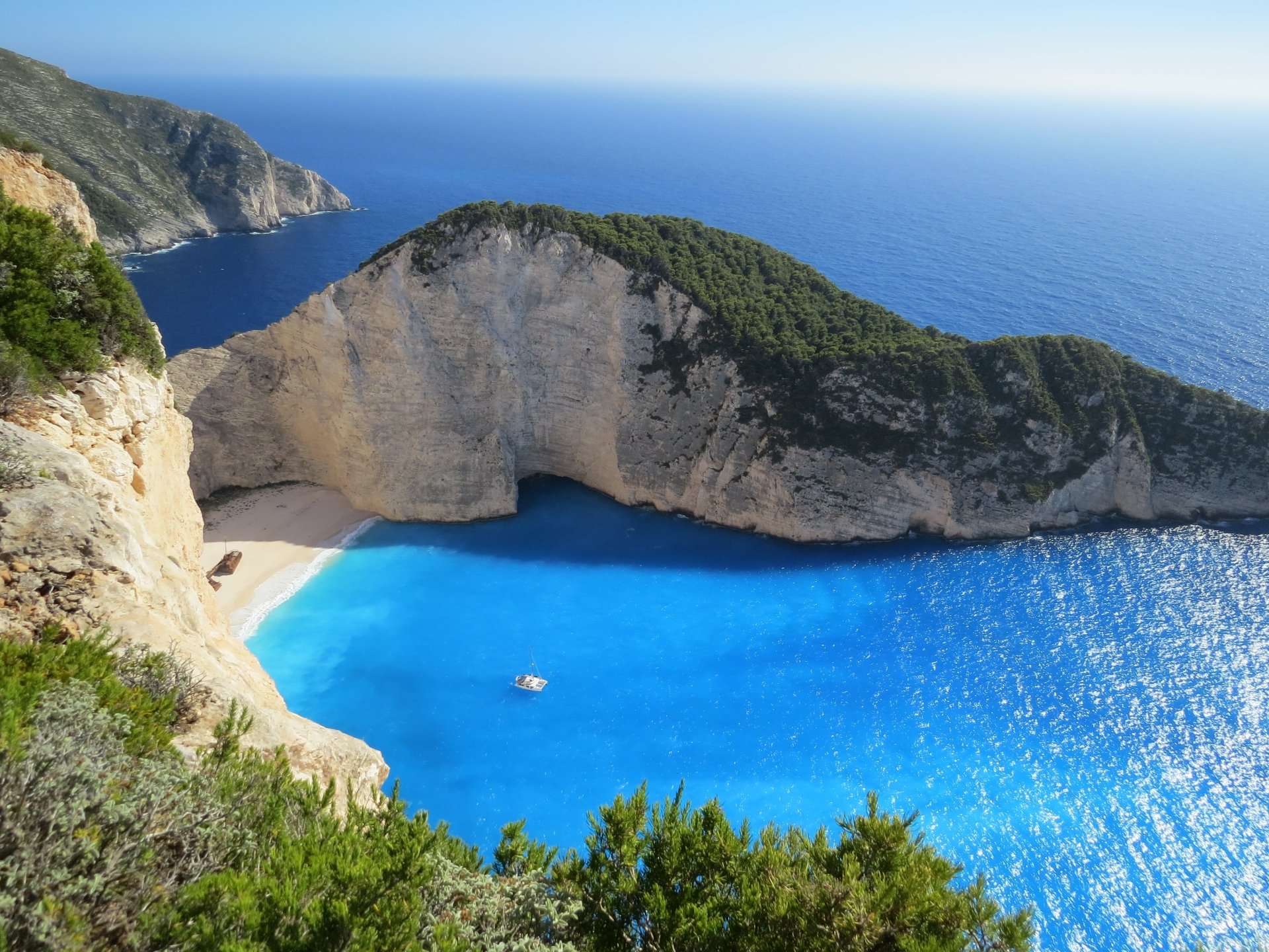 A stunning 4K Ultra HD wallpaper of Zakynthos coastline, showcasing a pristine beach with turquoise sea and lush greenery under a clear blue sky.