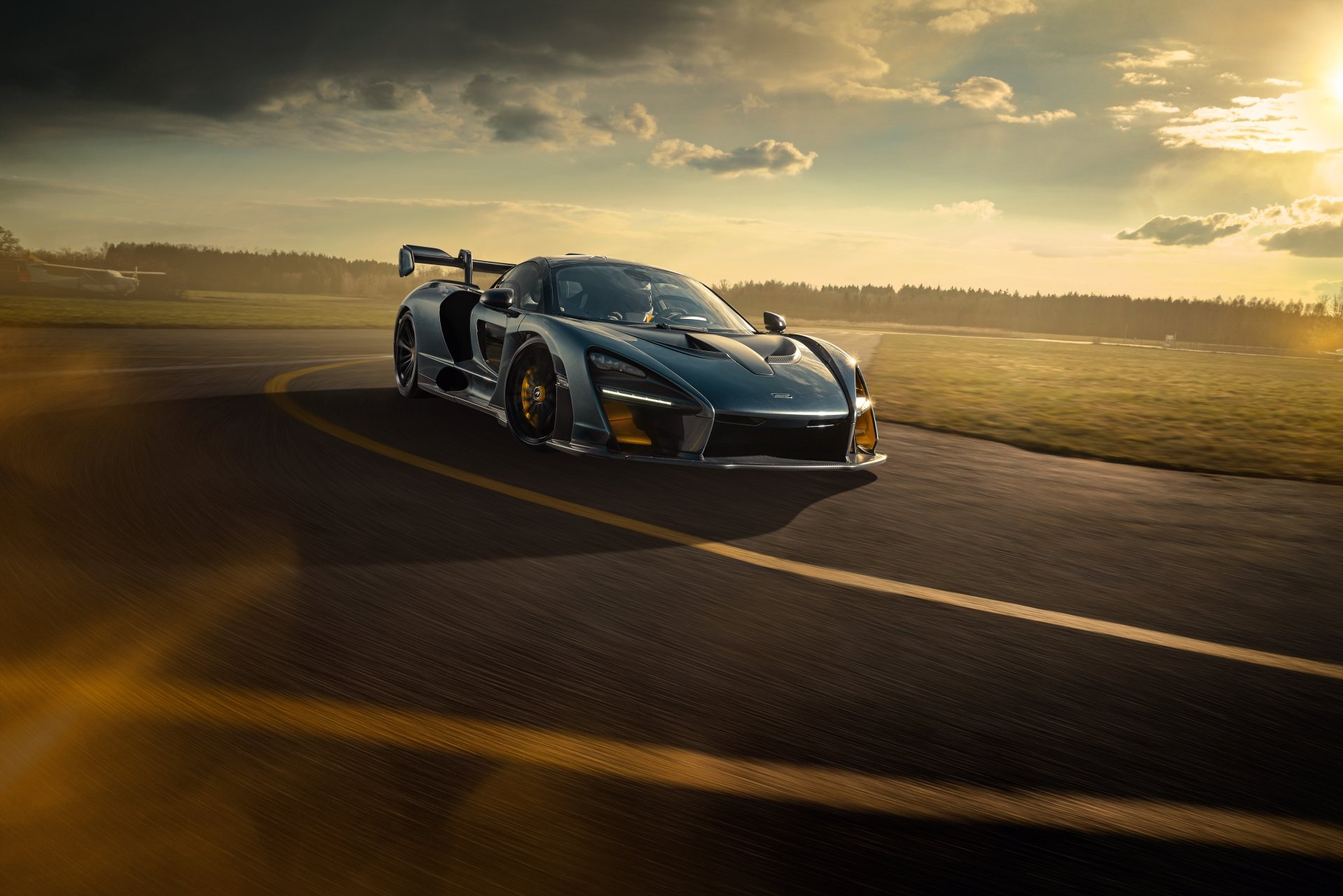 A sleek McLaren Senna supercar speeds on a race track at sunset, captured in stunning 8K Ultra HD as a dynamic PC desktop wallpaper background.