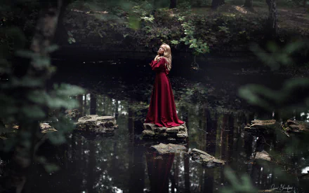 Blonde model in a flowing red dress stands on a rock in a dark forest pond, creating a moody HD PC desktop wallpaper/background.
