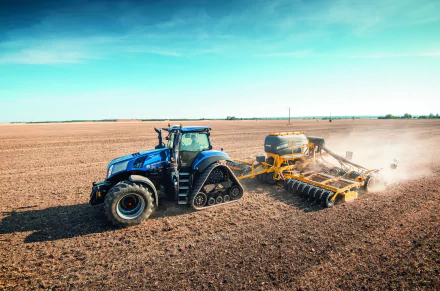 HD desktop wallpaper featuring a blue New Holland tractor with tracks working on a vast farmland under a clear blue sky.