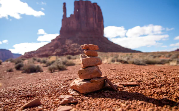 4K Ultra HD desktop wallpaper of a desert landscape featuring stacked stones in the foreground and a towering rock formation under a bright blue sky.