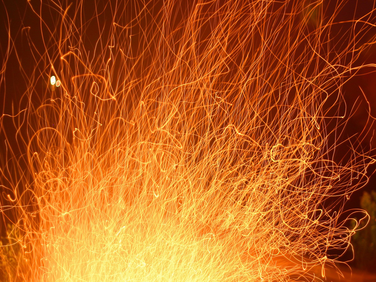 HD desktop wallpaper featuring vibrant, dynamic streaks of fire sparks captured in a long-exposure photography shot against a dark background.